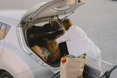 Charging electro car at the electric gas station. Woman standing by the car. Lady with foodstuff.
